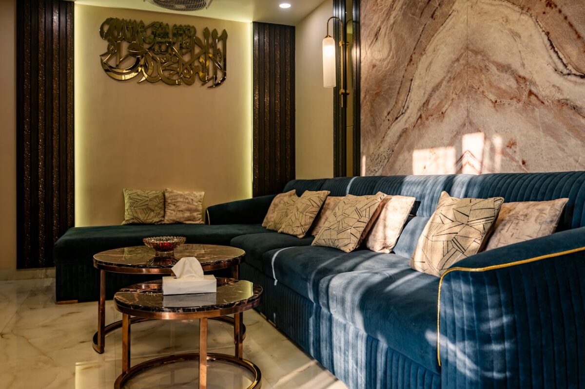 Elegant indoor lounge with a blue velvet sofa, decorative pillows, and marble walls featuring ambient lighting.