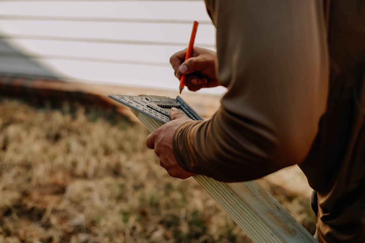 Carpenter measuring wood with a square outdoors, showcasing precise craftsmanship and manual labor.