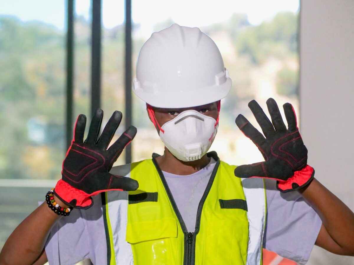 Construction worker wearing PPE gear including hardhat, gloves, and mask indoors.